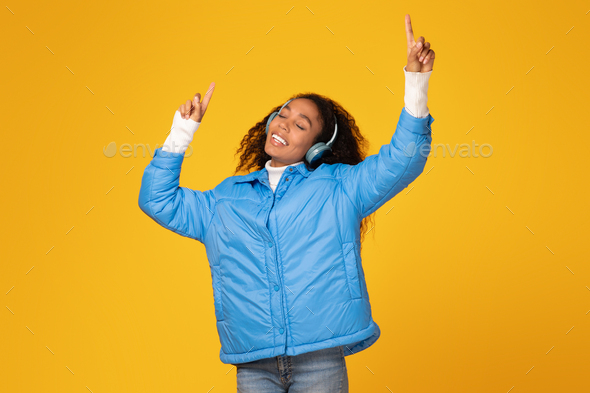 Excited black lady dances in headphones, yellow background