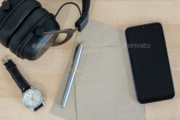 Top view wooden office desk with smart phone, headphones, watch, pen and recycled paper.