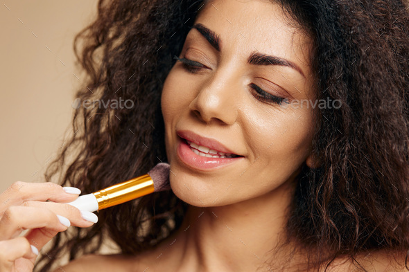 MAKEUP ARTIST CONCEPT. Enjoyed tanned awesome curly Latin lady hold makeup brush after makeup visage