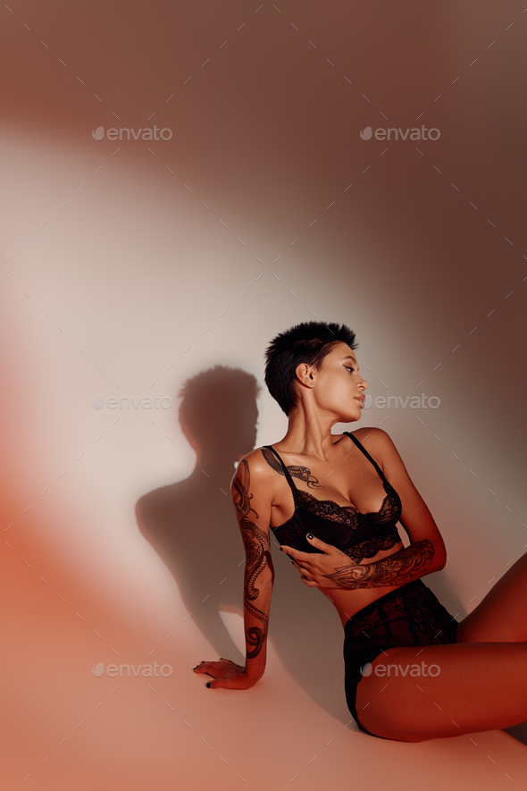 tattooed brunette woman in sexy lingerie sitting on red background with shadow