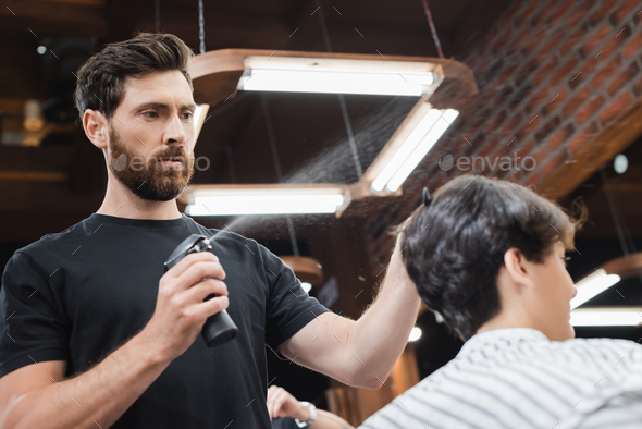 Barber's hands spray the little boy's hair with a spray gun. Stock