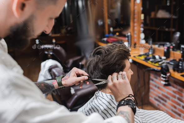 Blurred barber cutting hair of man in hairdressing cape in barbershop ...