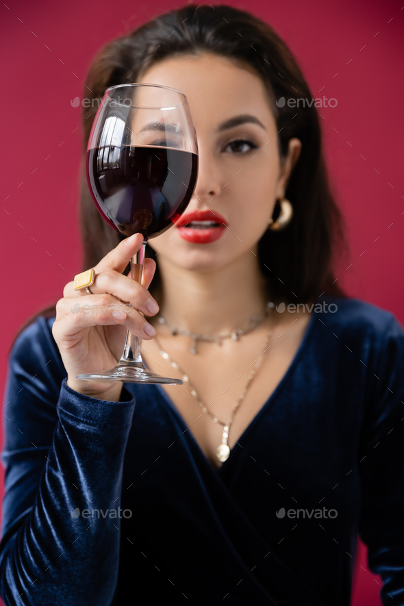 elegant woman obscuring face with glass of wine isolated on red