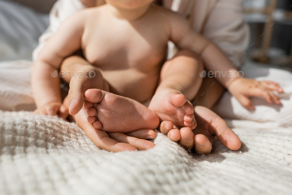 cropped view of mother holding in hands tiny bare feet of infant daughter  in bedroom Stock Photo by LightFieldStudios