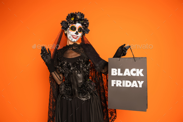 happy woman in traditional santa muerte makeup and costume holding black friday shopping bag