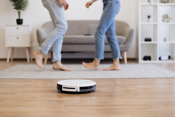Cleaning robot dusting off floor when young couple moving to music