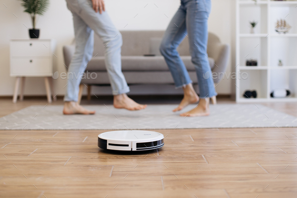 Cleaning robot dusting off floor when young couple moving to music