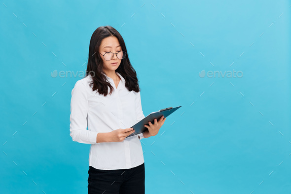 Focused cute Asian businesswoman in classic office dress code holds folder tablet read resume of