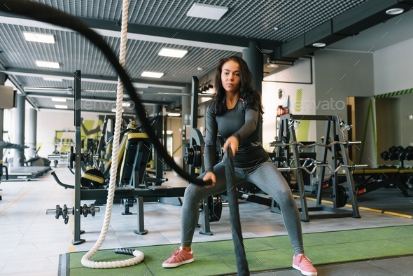 Fitness on the ropes. Beautiful female in gym working out with rope. Young woman training hard