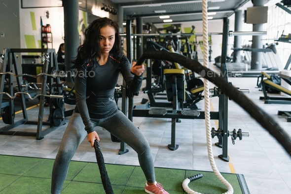 Fitness on the ropes. Beautiful female in gym working out with rope. Young woman training hard