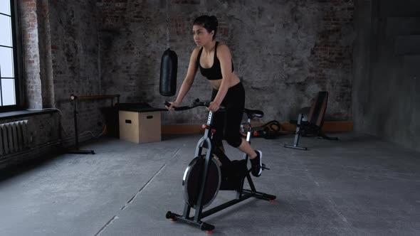 Young Athletic Indian Asian Woman Trains on a Bicycle Dressed in Sportswear Black Top  alt