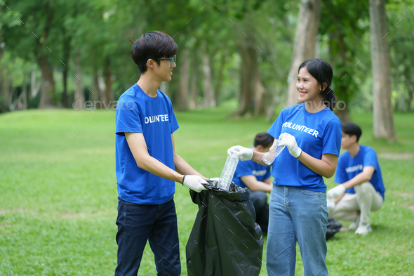 A group of Asian volunteers pick up trash on the lawn after an outdoor activity.