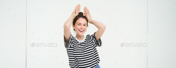 Young woman laughing, showing animal floppy ears gesture with hands on top of head, smiling and