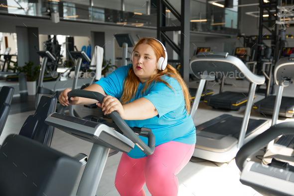Tired young woman with obesity on treadmill during training workout