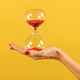 Unrecognizable woman holding hourglass in hand against yellow backdrop - PhotoDune Item for Sale