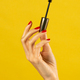 Unrecognizable young woman holding mascara in hand against yellow backdrop - PhotoDune Item for Sale