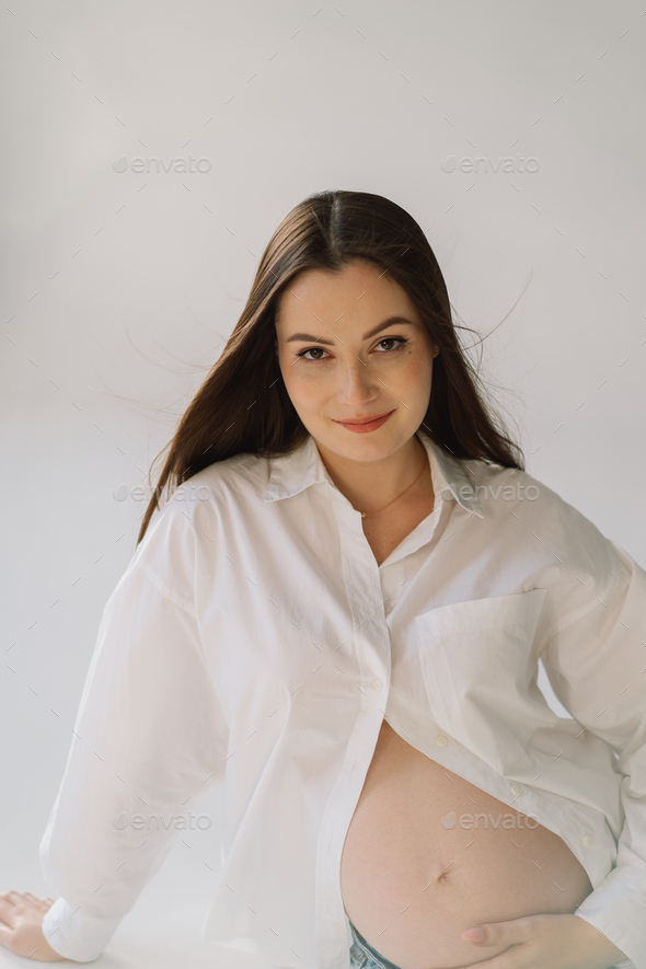 Cute young Pregnant girl sitting on the white studio in warm light Stock  Photo by StiahailoAnastasiia