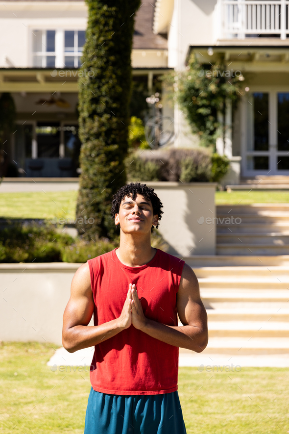 Happy biracial fit man practicing yoga meditation standing in sunny garden, copy space