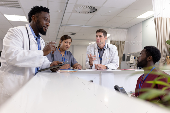 Busy diverse doctors and medical staff talking at reception desk of hospital ward, copy space
