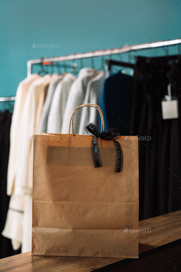 Lady hangs a black bow on a paper bag in front of a rack of clothes on hangers