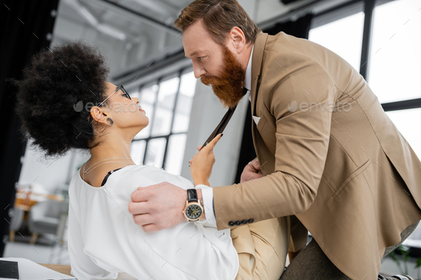 Side View Of Curly African American Woman Pulling Tie Of Bearded