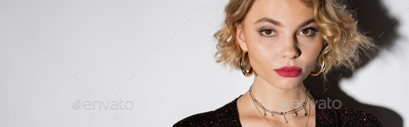 portrait of blonde young woman in golden hoop earrings and silver necklace looking at camera on