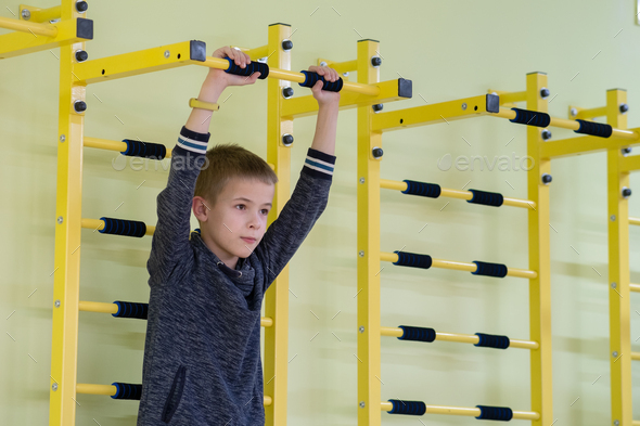 Young child boy exercising on a wall ladder bar inside sports gym room in a school.
