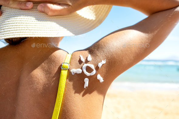 Back view of young woman tanning at the beach with sunscreen cream in sun  shape Stock Photo by bilanol