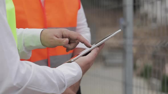 Close Up of Architect Hands Using Tablet Near Construction Site. The Builder and Architect Man Are alt