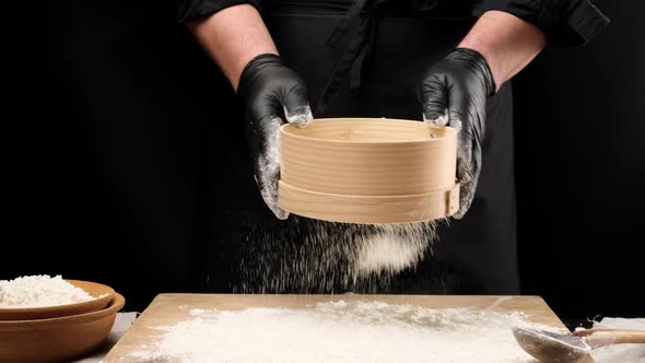 chef in black latex gloves and black clothes holds a round wooden sieve alt