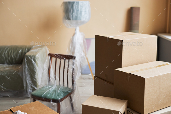 Stack of boxes standing on the floor against furniture covered with cellophane