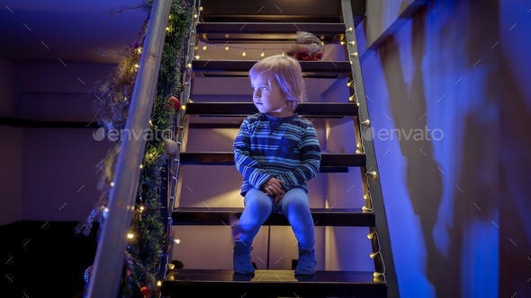 Little boy sitting on stairs decorated for Christmas or New Year and looking at police lights