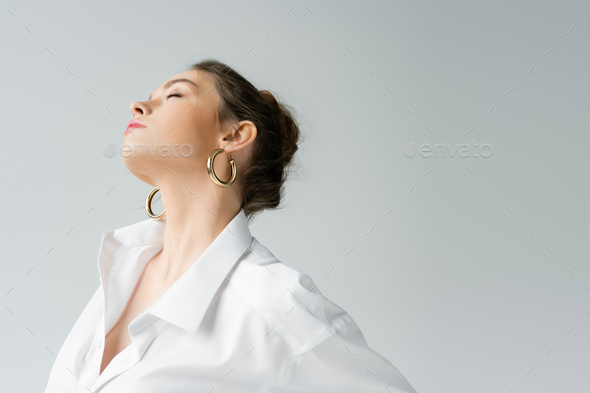 young sensual woman in white shirt and hoop earrings posing isolated on grey