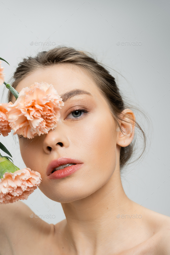 young woman with perfect skin and natural makeup obscuring face with peach carnations isolated on
