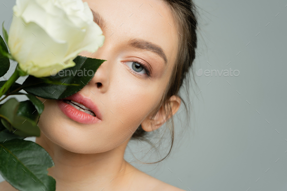 portrait of young woman with clean skin obscuring face with fresh rose and looking at camera