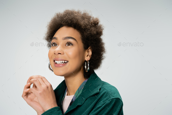 portrait of excited african american woman with curly brunette hair and hoop earrings looking away