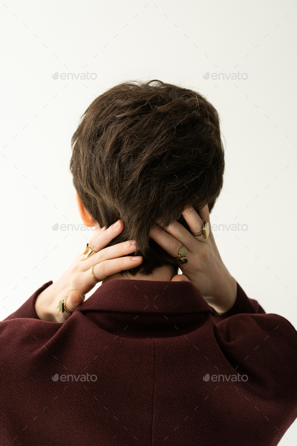 back view of brunette short haired woman in finger rings posing with hands behind neck isolated on