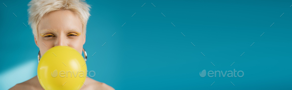 blonde albino woman with bright eye liner blowing bubble gum on blue background, banner