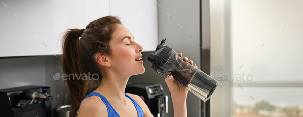 Close up portrait of sportswoman face, fitness girl drinks water from sport bottle and smiling