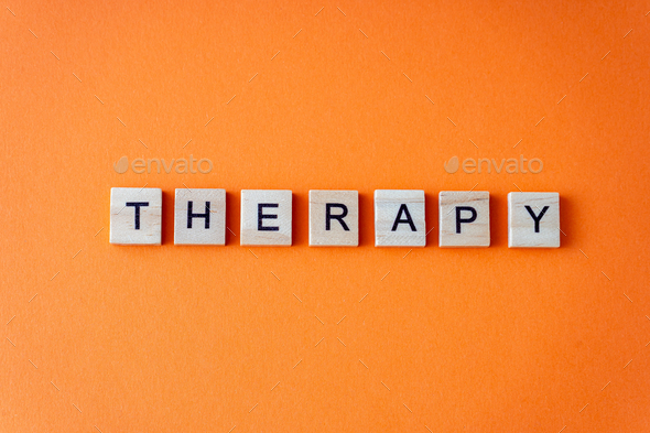 Word therapy. The phrase is laid out in wooden letters top view. Orange flat lay background