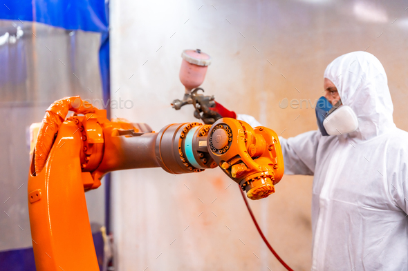 Industrial painter painting a robotic arm with spray