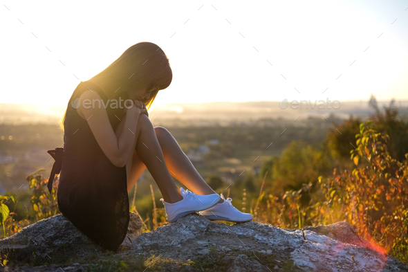 Young depressed woman in black short summer dress sitting on a