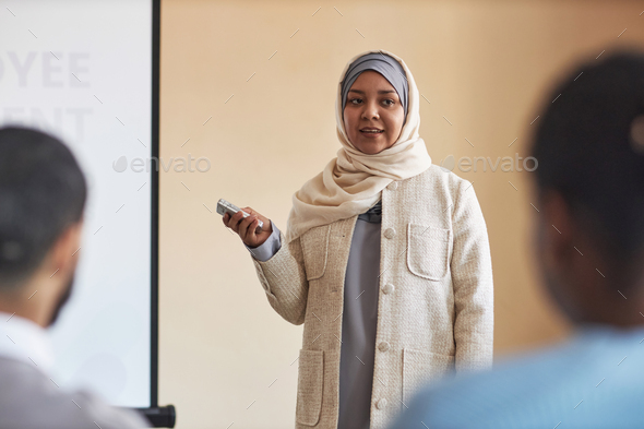 Young Muslim woman in hijab using laser pointer or switching slides
