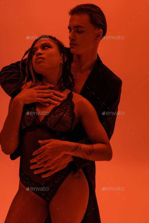 young and self-assured man in blazer hugging provocative and sexy african american woman with
