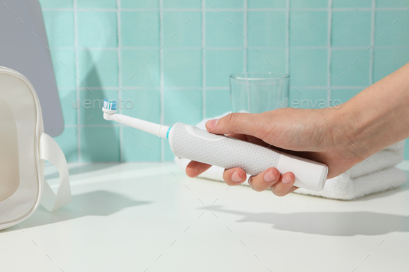 Electric toothbrush in hand, glass and mirror on blue background