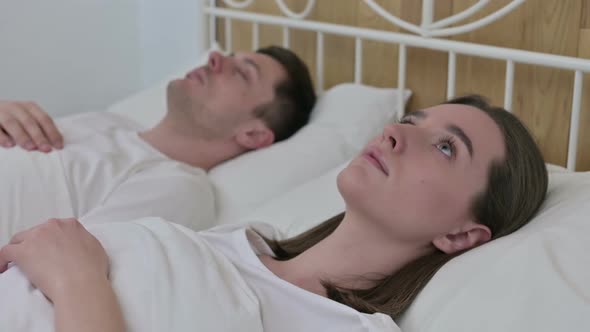 Beautiful Woman Awake in Bed Next to Sleeping Partner alt