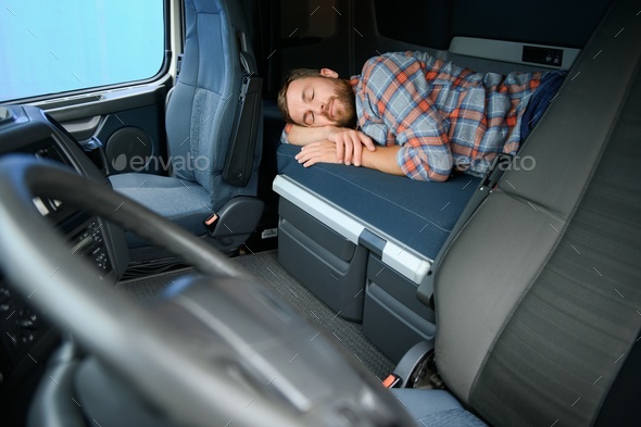 Truck driver sleeping on bed inside truck cabin interior. Trucker lifestyle.