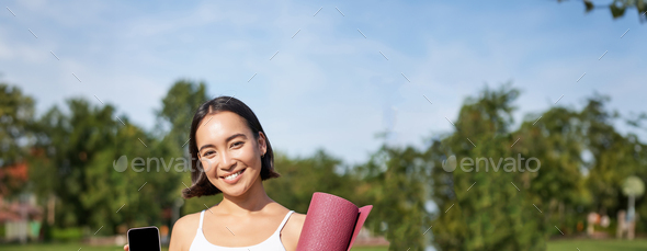 Excited fitness girl recommends application for sport and workout, shows phone screen, standing