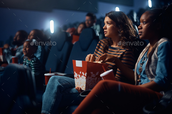 Young woman eating popcorn while watching sad movie in cinema.