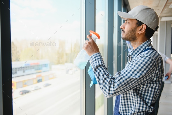 Indian Male professional cleaning service worker cleans the windows and shop windows